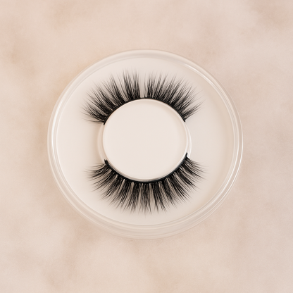 Pair of false eyelashes in a clear container on a beige background