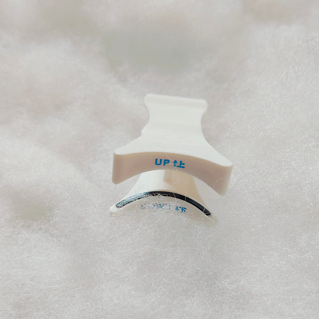 A white eyelash applicator with ergonomic design, lying on a textured surface.
